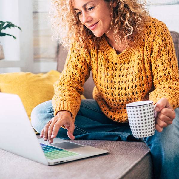 Young woman working on her laptop while she enjoys her coffee.