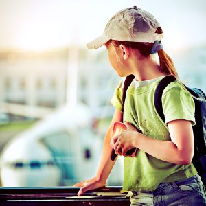 Young girl wearing a ball cap and blond pony tail, waiting to board her plane.