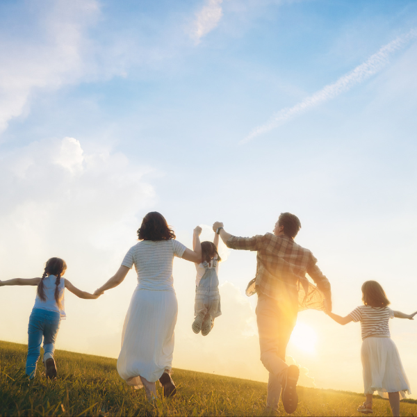 Family holding hands running along the beach as the sunsets.